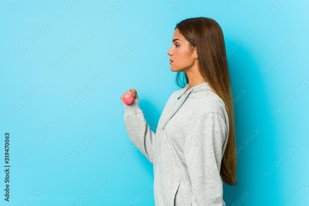 Young caucasian woman holding a dumbbell isolated on a blue background