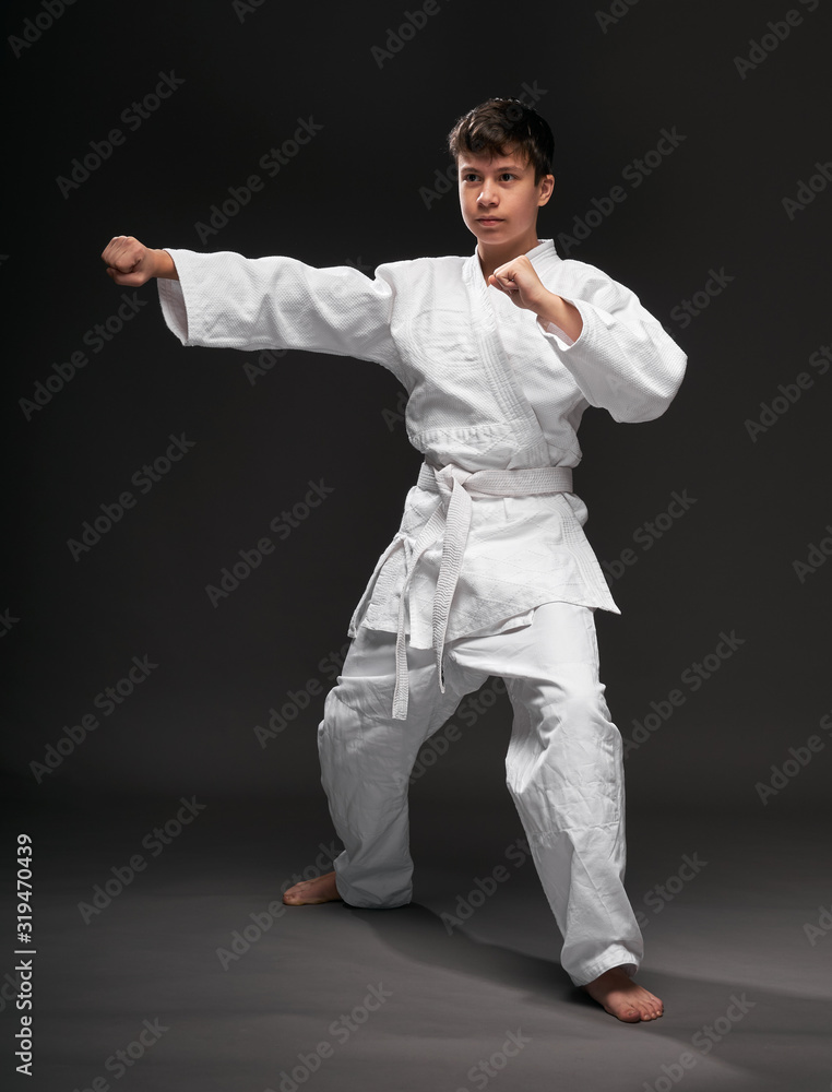a teenager dressed in martial arts clothing poses on a dark gray background, a sports concept a teenager dressed in martial arts clothing poses on a dark gray background, a sports concept
