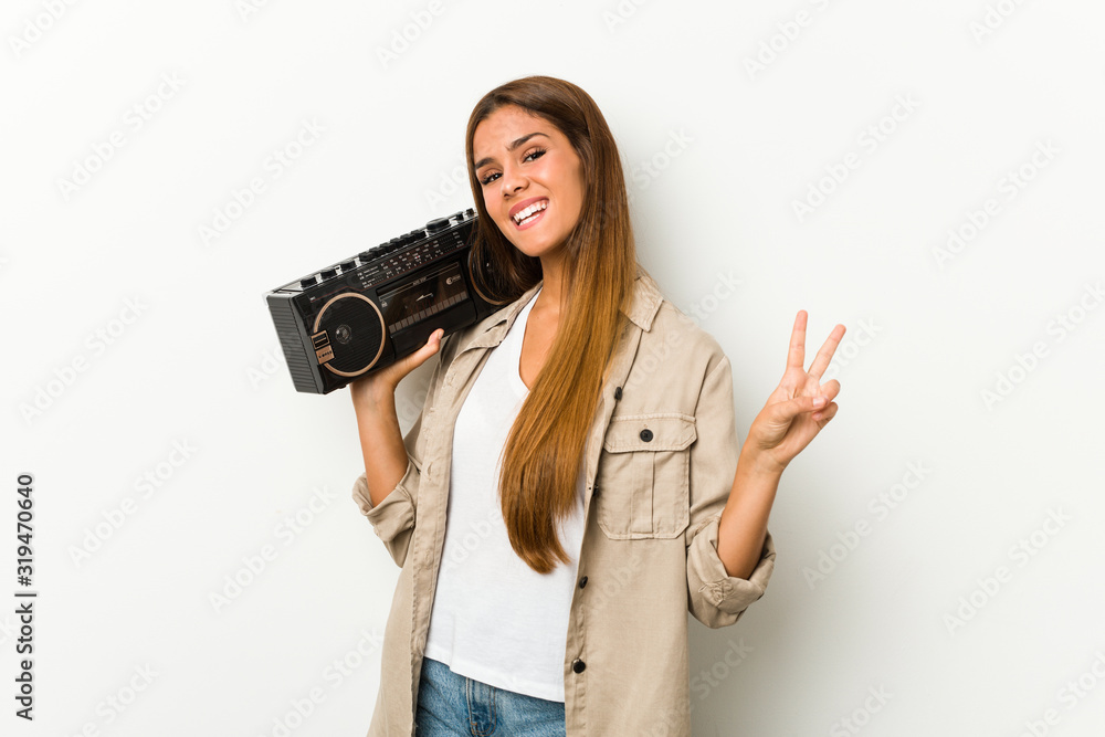 Young caucasian woman holding a guetto blaster joyful and carefree showing a peace symbol with fingers. Young caucasian woman holding a guetto blaster joyful and carefree showing a peace symbol with fingers.