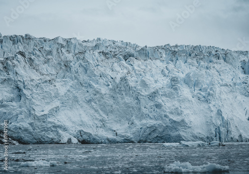 Close Up shot of huge Glacier wall. Large chunks of ice breaking off. Moody and overcast weather. Eqip Sermia Glacier called Eqi Glacier. Greenlandic ice cap melting because of global warming. © Mathias