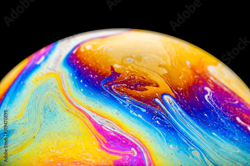 Rainbow soap bubble on an isolated black background. Close-up of the colorful surface. Poster blank