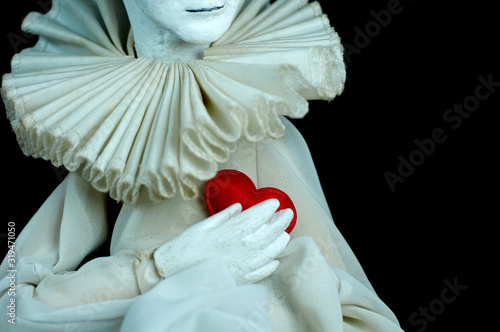 .Harlequin doll holds a small red heart for Valentine's Day on a black background. photo