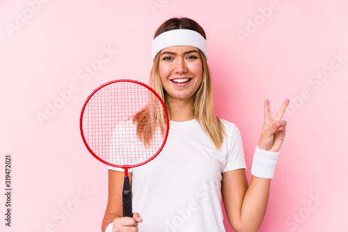 Young woman playing badminton isolated joyful and carefree showing a peace symbol with fingers.