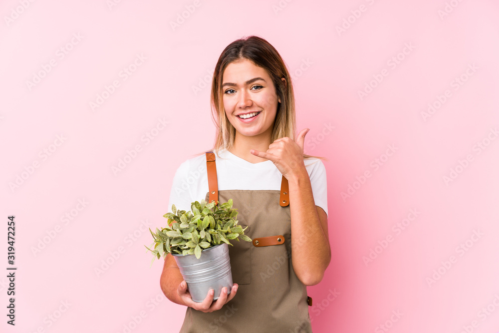 Young caucasian gardener woman in a pink background showing a mobile phone call gesture with fingers. Young caucasian gardener woman in a pink background showing a mobile phone call gesture with fingers.