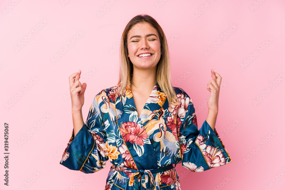 Young caucasian woman wearing pajamas crossing fingers for having luck Young caucasian woman wearing pajamas crossing fingers for having luck