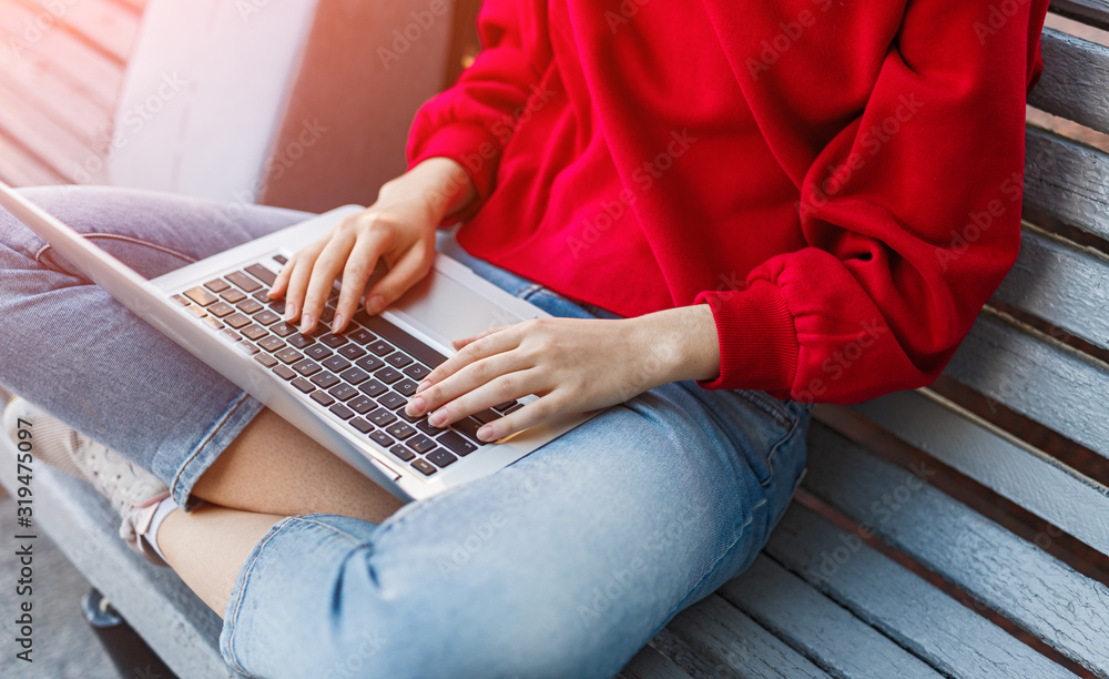 Naklejka premium Young woman sitting on bench and working on laptop