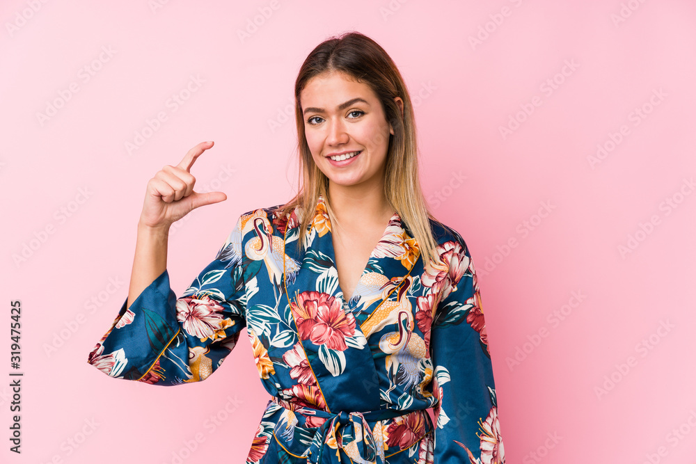 Young caucasian woman wearing pajamas holding something little with forefingers, smiling and confident. Young caucasian woman wearing pajamas holding something little with forefingers, smiling and confident.