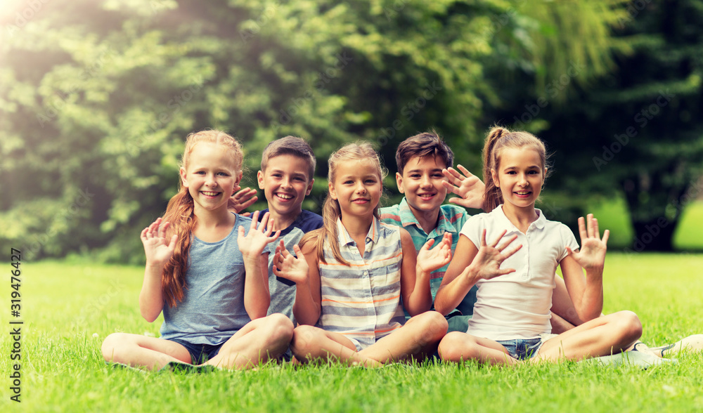 friendship, childhood, leisure and people concept - group of happy kids or friends waving hands in summer park