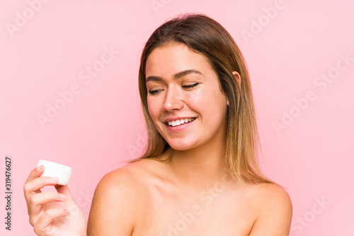 Young caucasian woman holding a moisturizer isolated smiling confident with crossed arms.