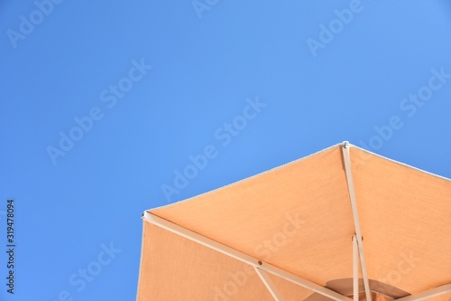 Part of beach folding umbrella on blue sky background. Summer background with sun parasol on blue sky backdrop. Summertime. Vacation concept. Vacation at the beach mock up. 