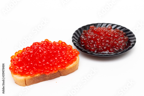 Red caviar on white bread and a black plate. On a white background