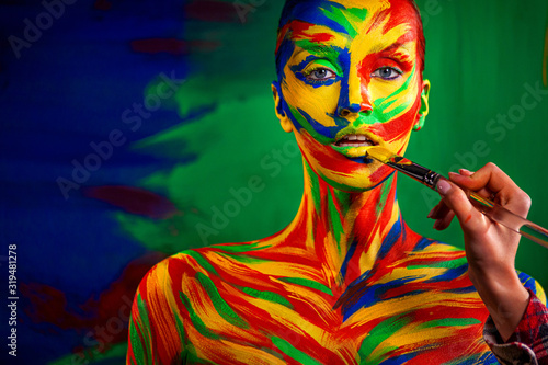 Color art face and body painting on woman for inspiration. Abstract portrait of the bright beautiful girl with colorful make-up and bodyart.