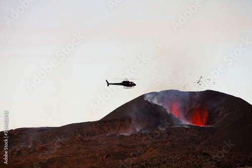 Canvas Print Helicopter flying over an erupting volcano on Iceland.