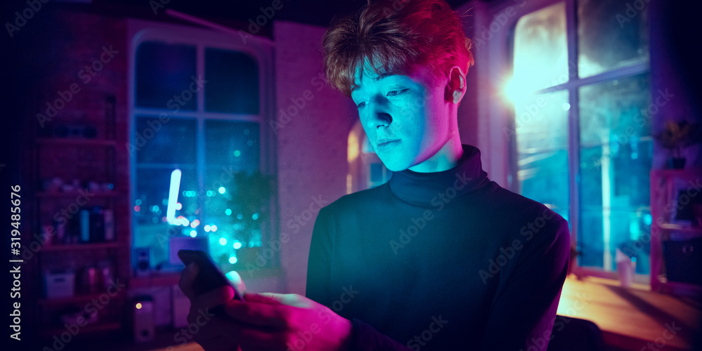 Calm, serious. Cinematic portrait of stylish redhair man in neon lighted interior. Toned like cinema effects in purple-blue. Caucasian model using smartphone in colorful lights indoors. Flyer.