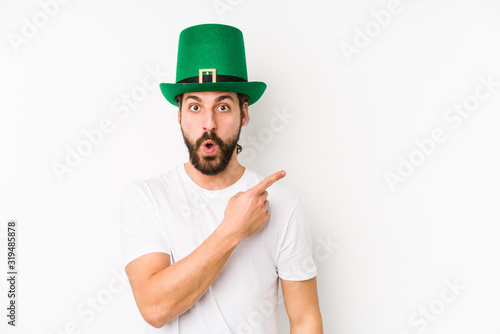 Young caucasian man wearing a saint patricks hat isolated pointing to the side