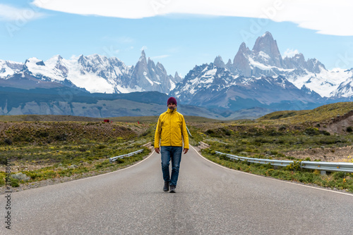 Alone hiker with yellow jacket walking on an empty road with the Mount Fitz Roy on the background. Patagonia, Argentina