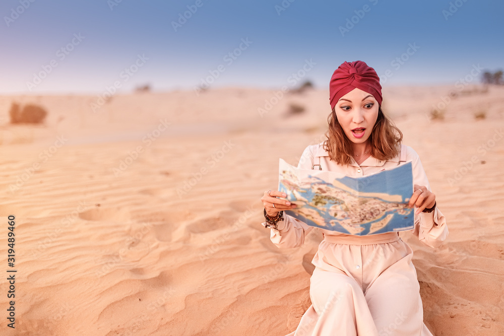 Asian woman wearing turban reading map in Sahara desert in Africa. Travel and tourism concept