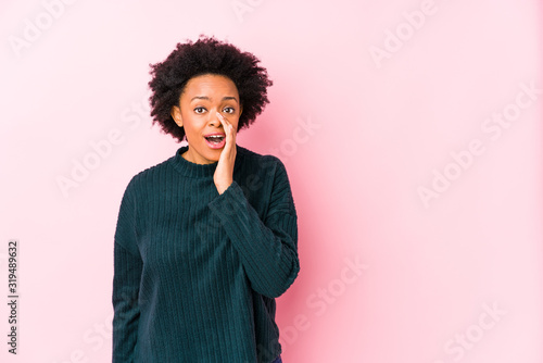 Middle aged african american woman against a pink background isolated is saying a secret hot braking news and looking aside © Asier