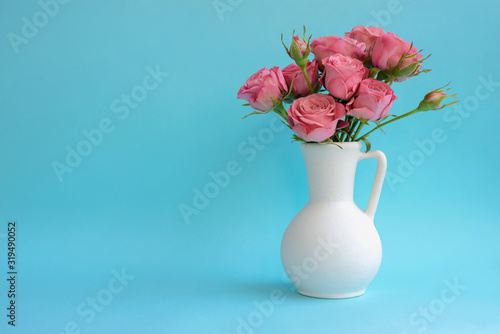 Bouquet of pink roses in white vase on blue background. Copy space
