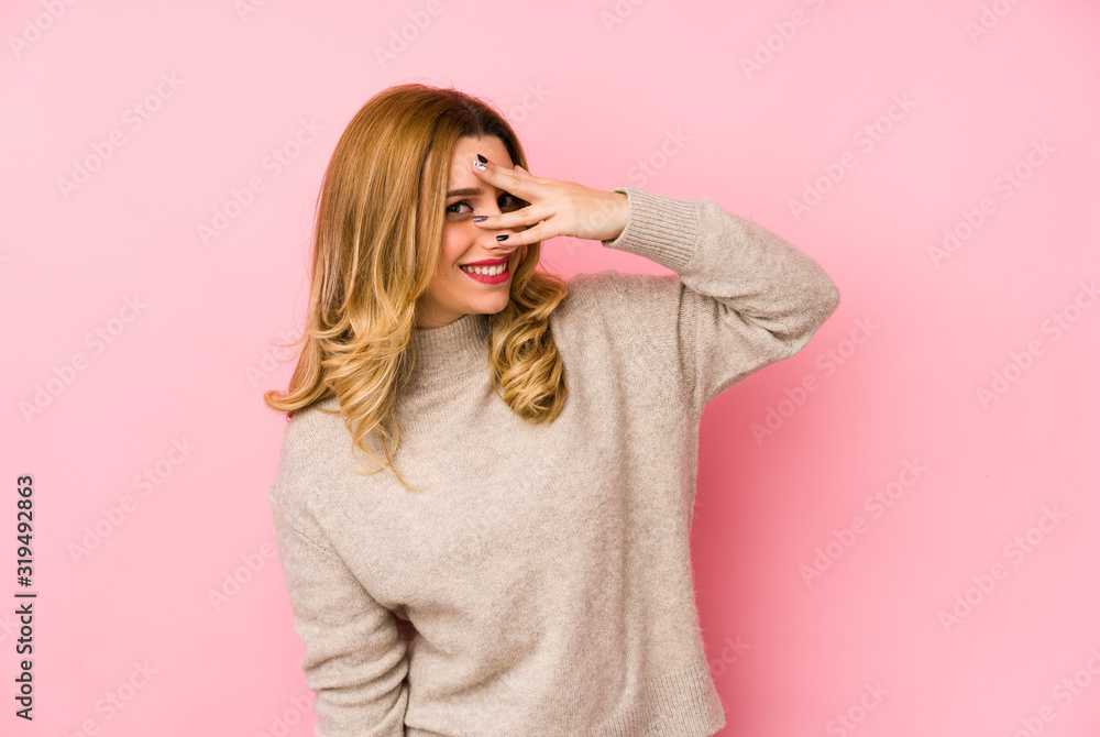 Young blonde cute woman wearing a sweater isolated blink at the camera through fingers, embarrassed covering face. Young blonde cute woman wearing a sweater isolated blink at the camera through fingers, embarrassed covering face.