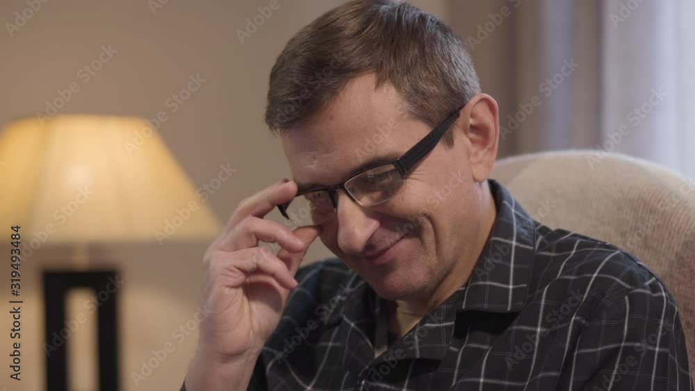 Close-up portrait of happy Caucasian middle aged man in eyeglasses looking at something down and smiling. Positive adult man guy spending evening at home. Leisure, happiness, lifestyle. Close-up portrait of happy Caucasian middle aged man in eyeglasses looking at something down and smiling. Positive adult man guy spending evening at home. Leisure, happiness, lifestyle.
