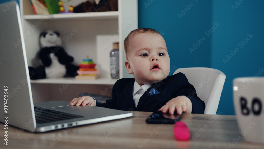 Close up view of extremely cute baby boss in formal suit sitting by the laptop and taking the phone of the table. Toddler shooting, indoors. Modern kids office. Success, happy childhood, cuteness Close up view of extremely cute baby boss in formal suit sitting by the laptop and taking the phone of the table. Toddler shooting, indoors. Modern kids office. Success, happy childhood, cuteness