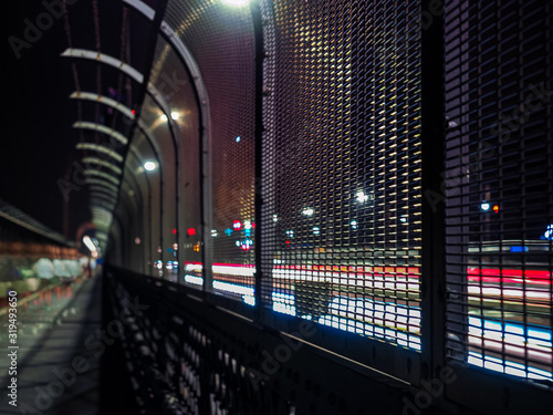 Blurred metal fence with blurred motion car light trails passing by and a night cityscape background.