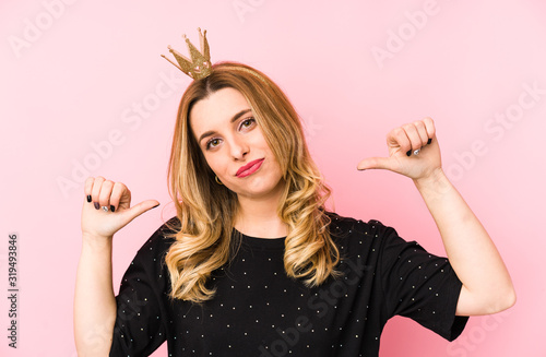 Young blonde woman wearing a crown isolated feels proud and self confident, example to follow.