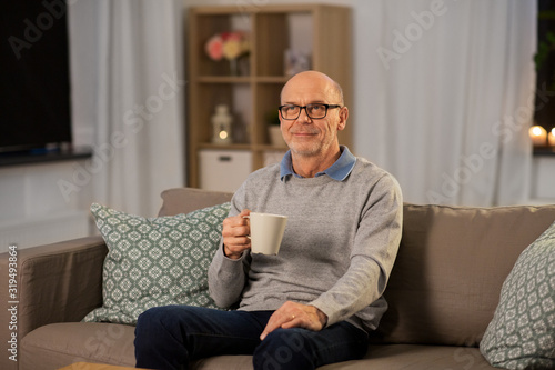 old age, drink and people concept - happy senior man with cup of tea at home in evening
