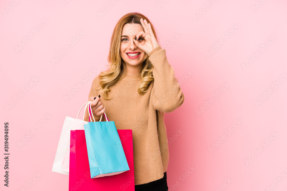 Young blonde woman holding shopping bags isolated excited keeping ok gesture on eye. Young blonde woman holding shopping bags isolated excited keeping ok gesture on eye.