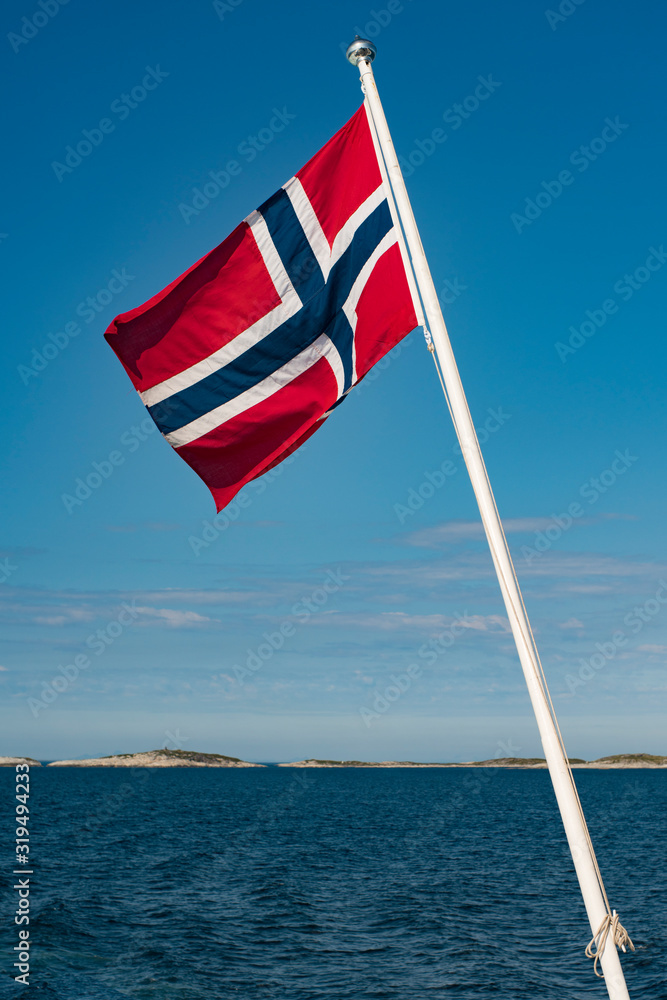 Norway Full National Flag on Flagpole With Lofoten Background and clear blue sky.