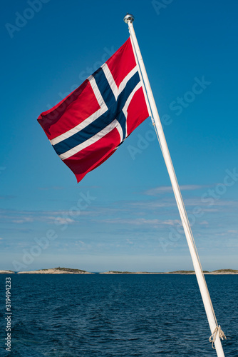 Norway Full National Flag on Flagpole With Lofoten Background and clear blue sky.