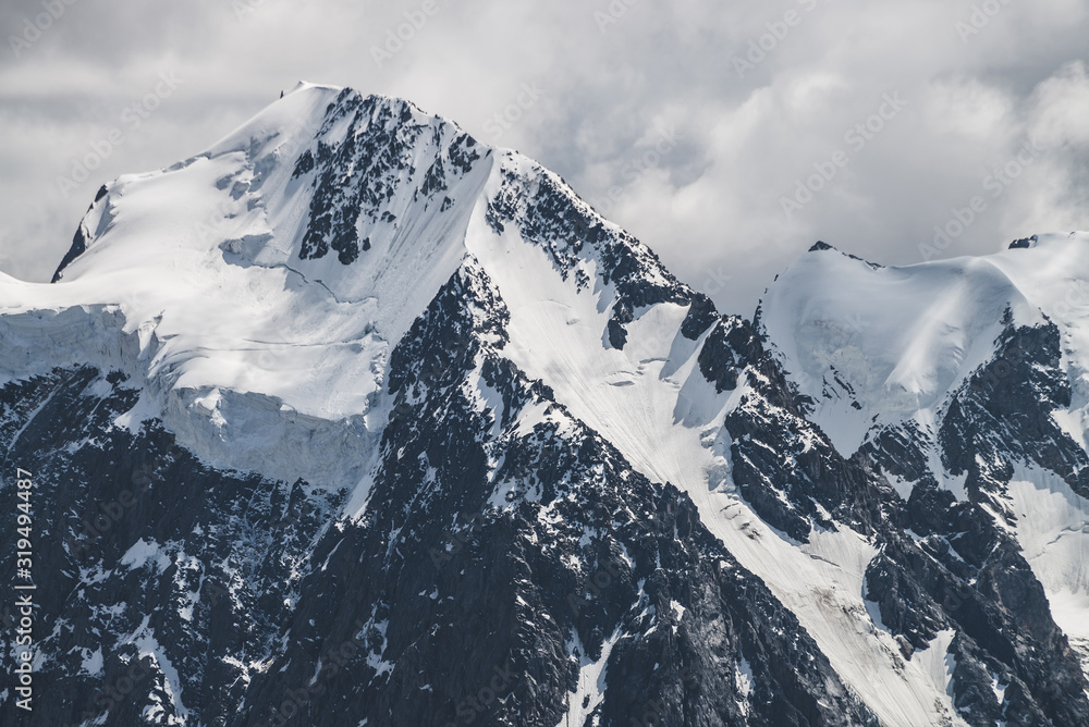 Atmospheric minimalist alpine landscape with massive hanging glacier on snowy mountain peak. Big balcony serac on glacial edge. Cloudy sky over snowbound mountains. Majestic scenery on high altitude.
