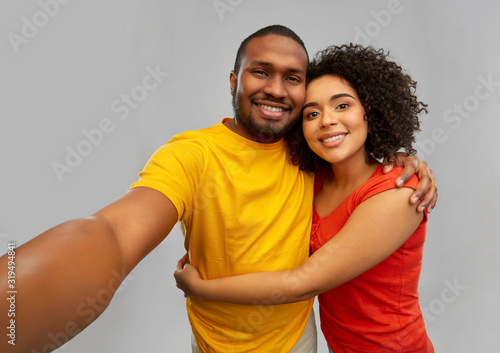 technology and people concept - happy smiling african american couple taking selfie over grey background