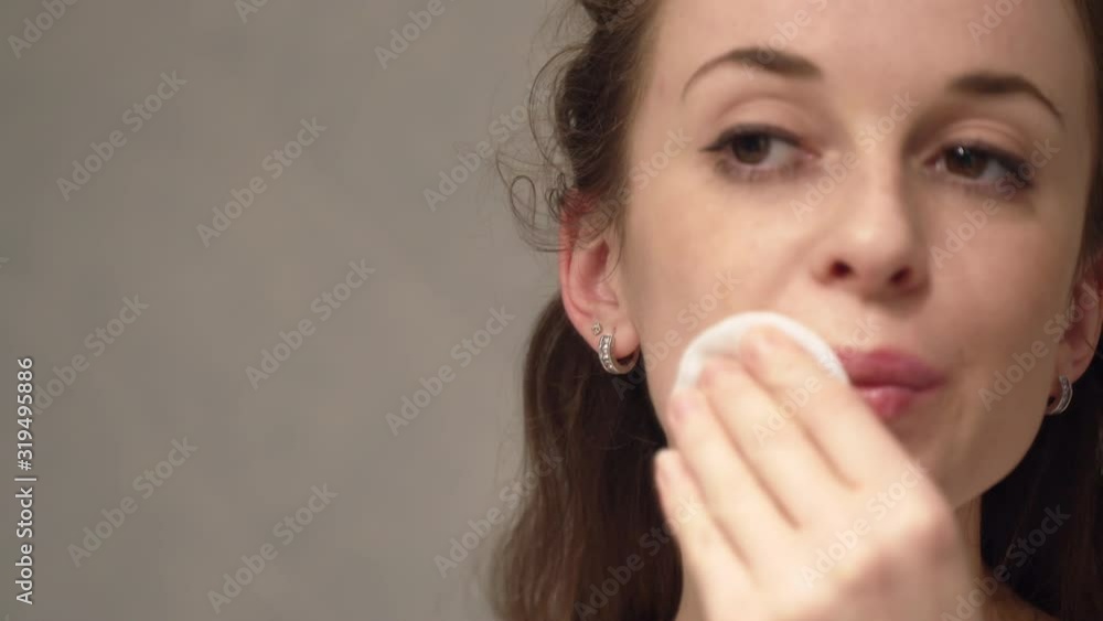 Tired smiling girl removing her daily make-up with cotton pad. Facial hygiene Tired smiling girl removing her daily make-up with cotton pad. Facial hygiene