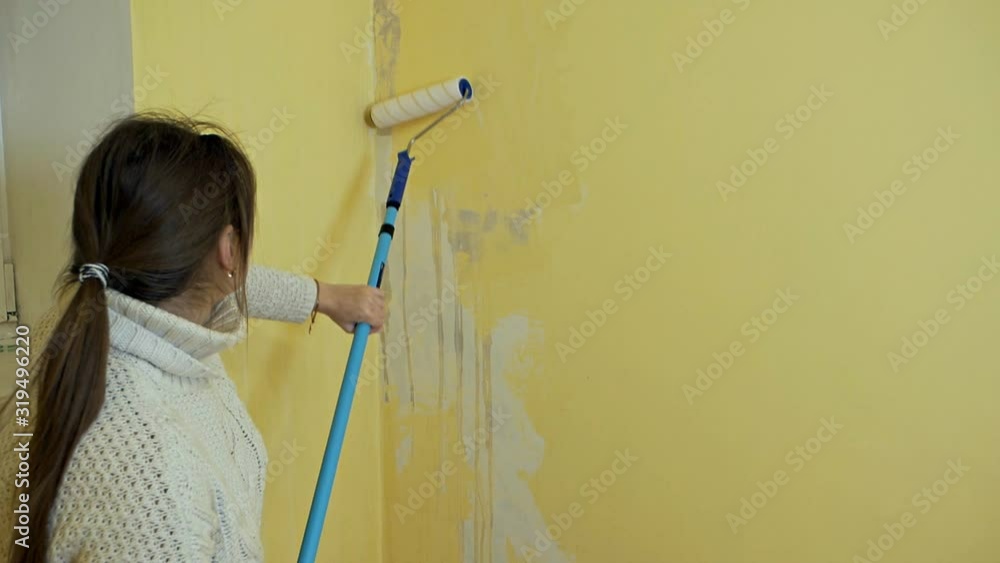 A self-taught girl prepares a wall for painting with a construction roller. A girl works she processes a yellow wall with a construction roller before painting. A self-taught girl prepares a wall for painting with a construction roller. A girl works she processes a yellow wall with a construction roller before painting.