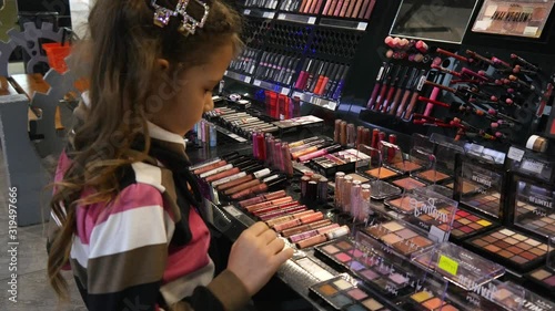 A Girl Kid chose cosmetics lipsticks, eye shadows in a Store