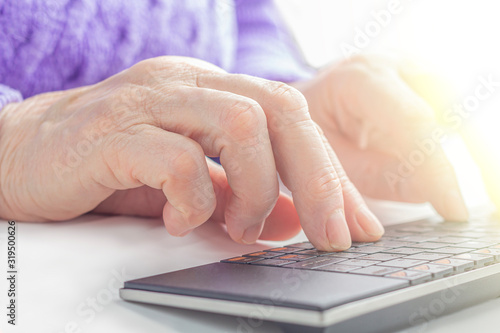 Elderly woman's hands typing on a PC keyboard close up. Pensioner working from home. The concept of learning seniors to computer literacy or internet skills.