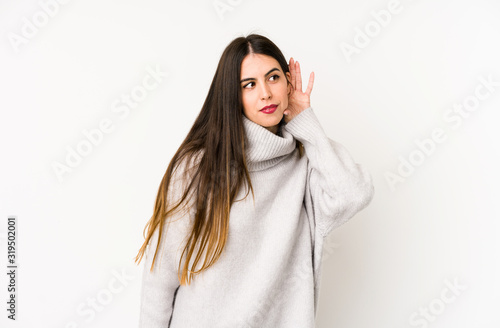 Young caucasian woman isolated on a white background trying to listening a gossip.