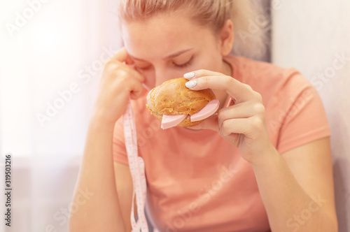 An overweight girl is eating a sandwich and holding a centimeter-long ribbon. Junk food. Selective focus  film grain.