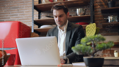 LVIV  UKRAINE - 10 MAY  2019  Serious young man looking at laptop making notes working with documents  doing paperwork  online research  focused businessman studying in internet writing down
