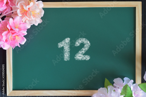 Number 12 write with white chalk, flowers on the board.
