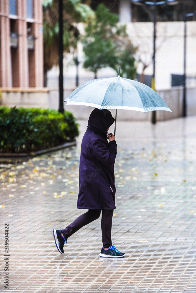 An adult man walked down the street of a city with a black umbrella on a rainy day.