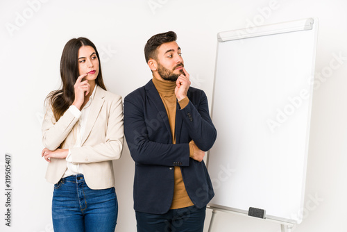 Young caucasian business couple isolated looking sideways with doubtful and skeptical expression.