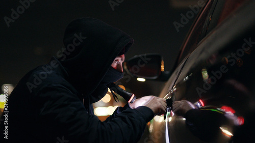 Photo Quickly robber checking breaking entering alarm shines a flashlight in a car sit