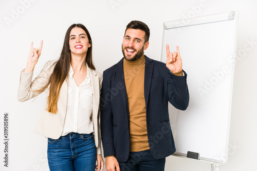 Young caucasian business couple isolated showing a horns gesture as a revolution concept.