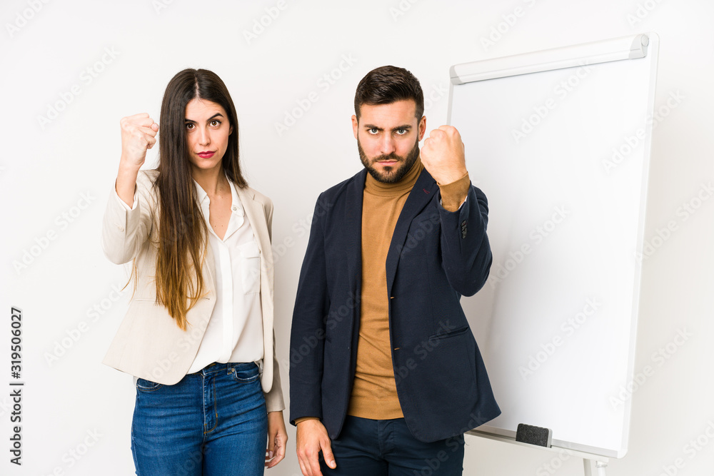 Young caucasian business couple isolated showing fist to camera, aggressive facial expression.