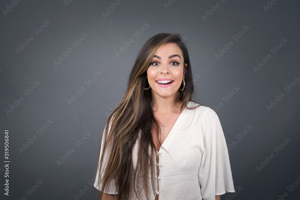 Emotive young blonde woman wears casual clothes, happy and excited to celebrate anniversary. Happy young woman has good mood stands against gray wall. Emotive young blonde woman wears casual clothes, happy and excited to celebrate anniversary. Happy young woman has good mood stands against gray wall.