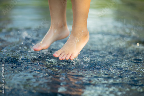 Heat in the city: close up of child's legs jumping at the water of street fountain © Alinsa