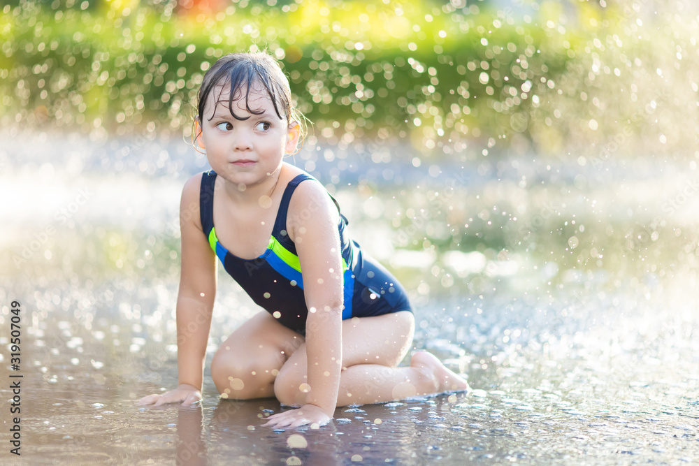 Obraz premium Little girl having fun playing with water in park at the water playground. Summer day